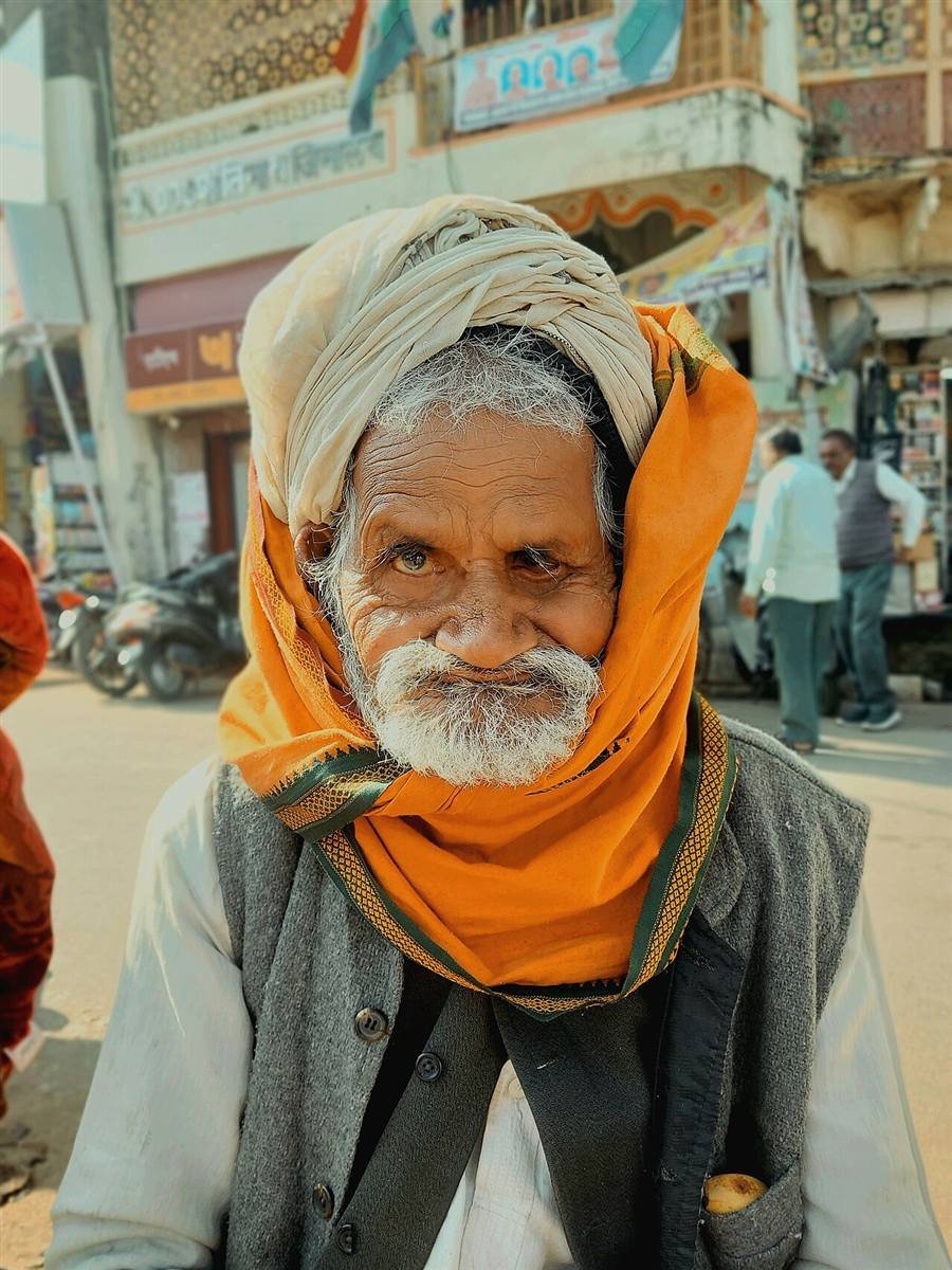 An elderly man in a traditional turban and shawl in a rural Indian marketplace